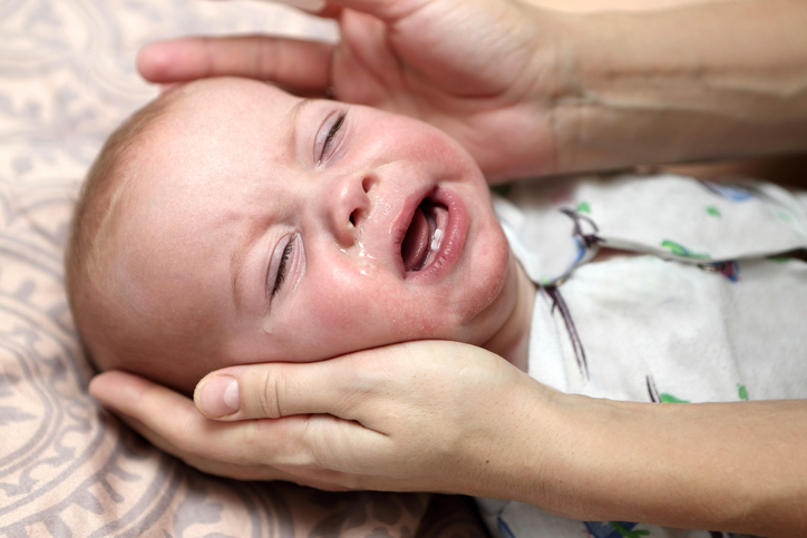 neklidný kojenec s prořezaným spodním párem zoubků a ruce matky mu drží hlavičku